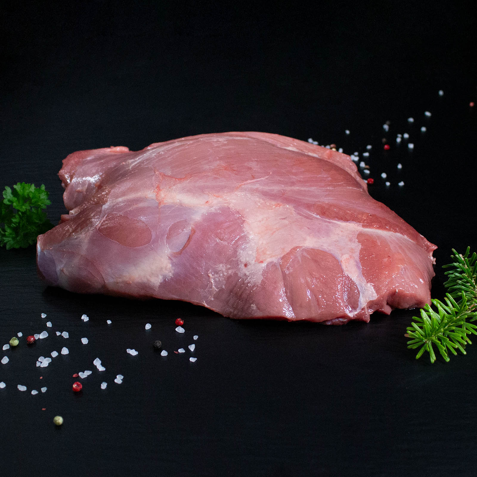 Rohe Frischlingskeule ohne Knochen mit Pfeffer, Salz und Chili auf dunklem Untergrund