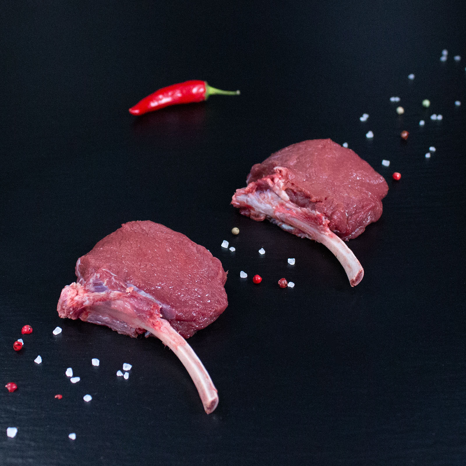Rohe Hirsch-Tomahawk-Steaks mit Kräutern und Gewürzen auf dunklem Untergrund