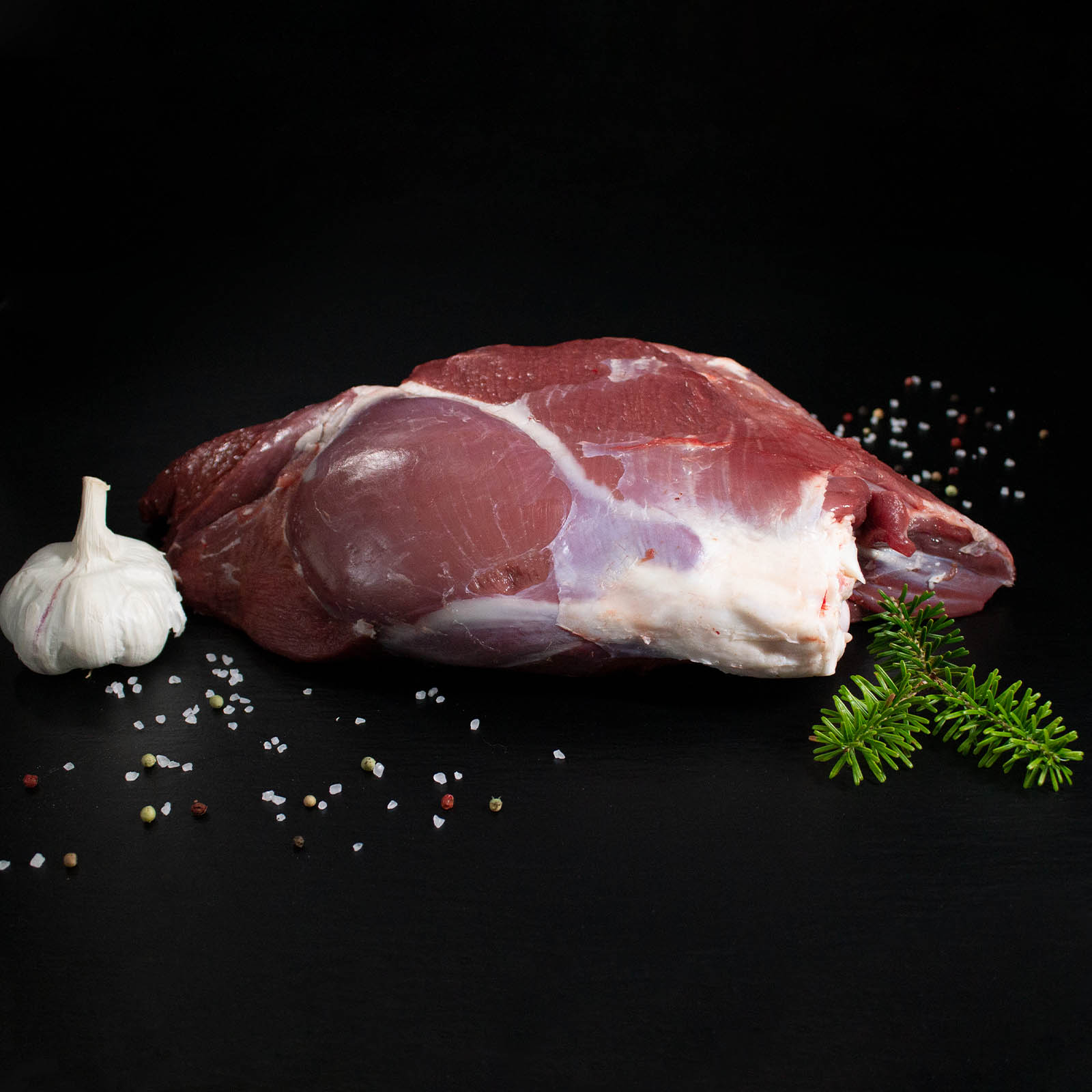 Rohe Hirschkalbskeule mit Knochen, Pfeffer, Salz und Chili auf dunklem Untergrund