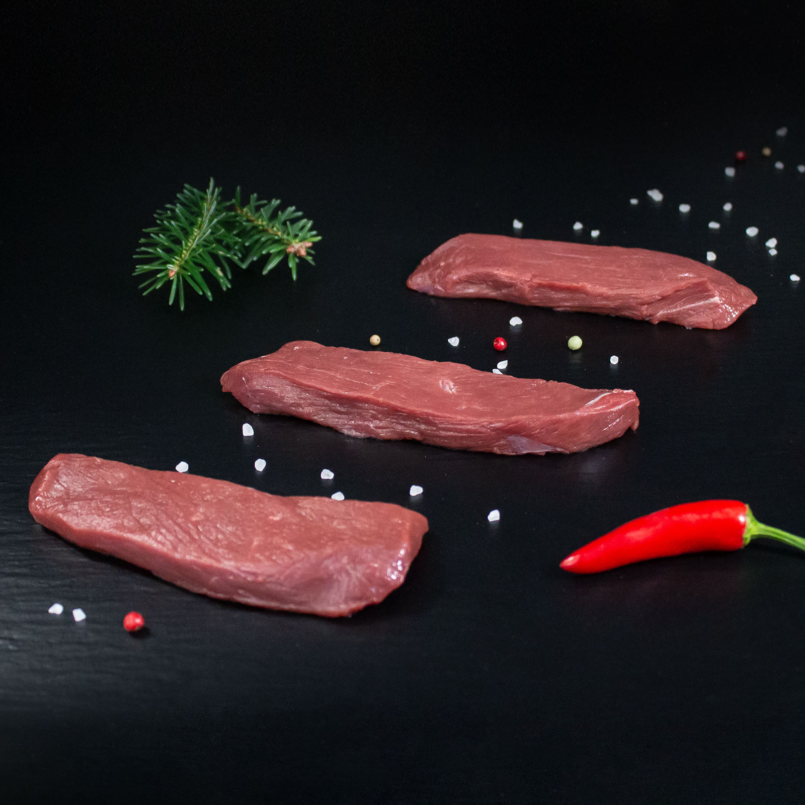 Rohe Rehsteaks mit Kräutern und Gewürzen auf dunklem Untergrund