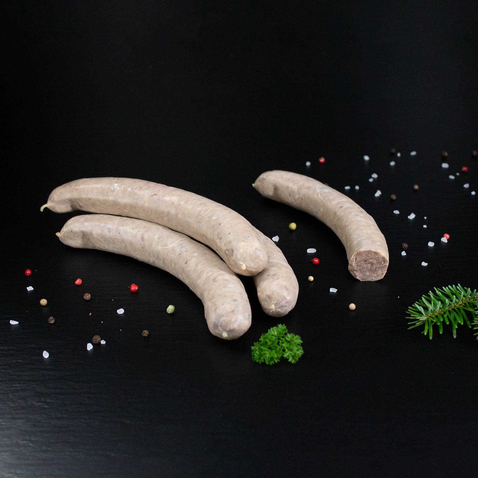 Wildbratwurst Natur (grob) mit Kräutern und Gewürzen auf dunklem Untergrund