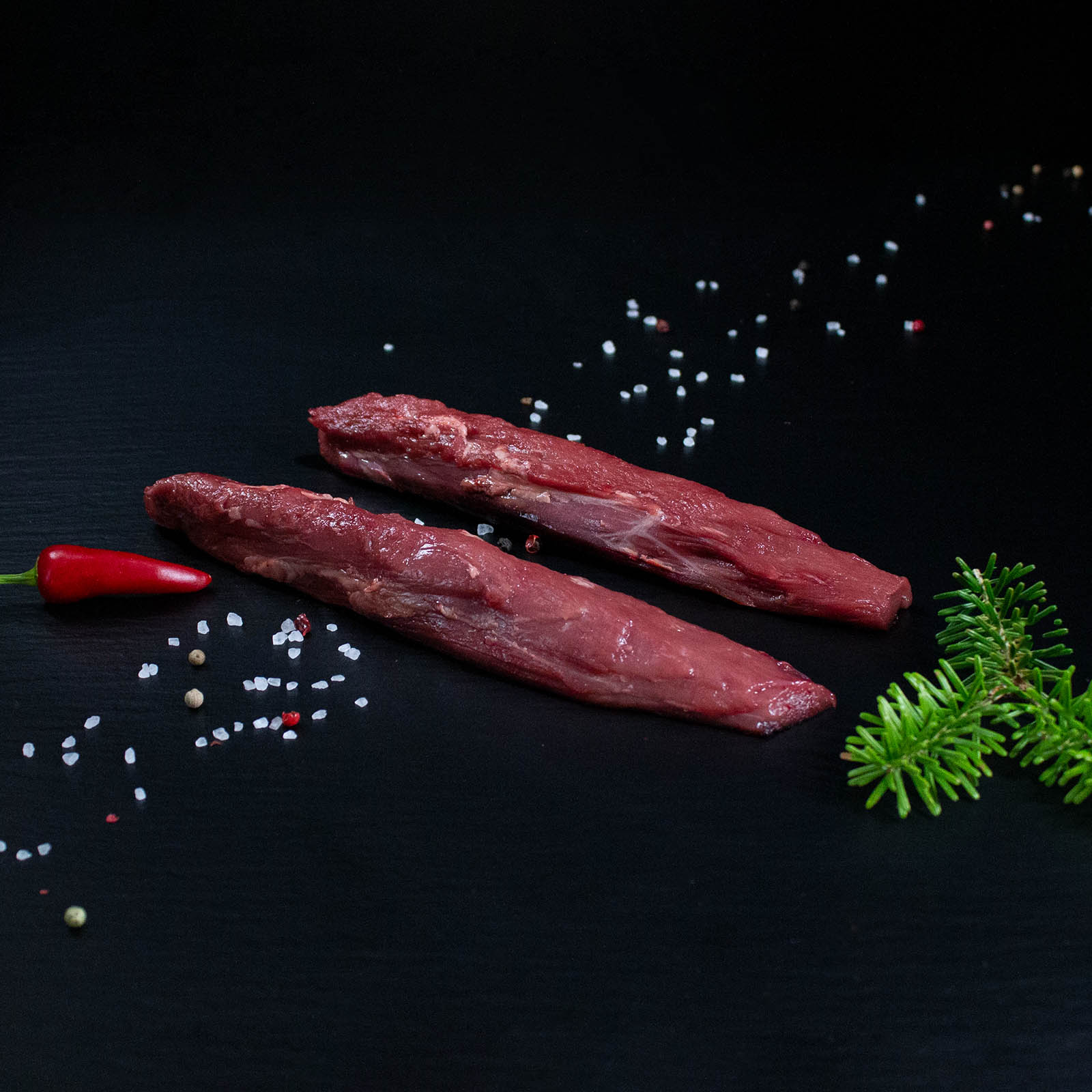 Rohe Wildschweinfilets mit Kräutern und Gewürzen auf dunklem Untergrund