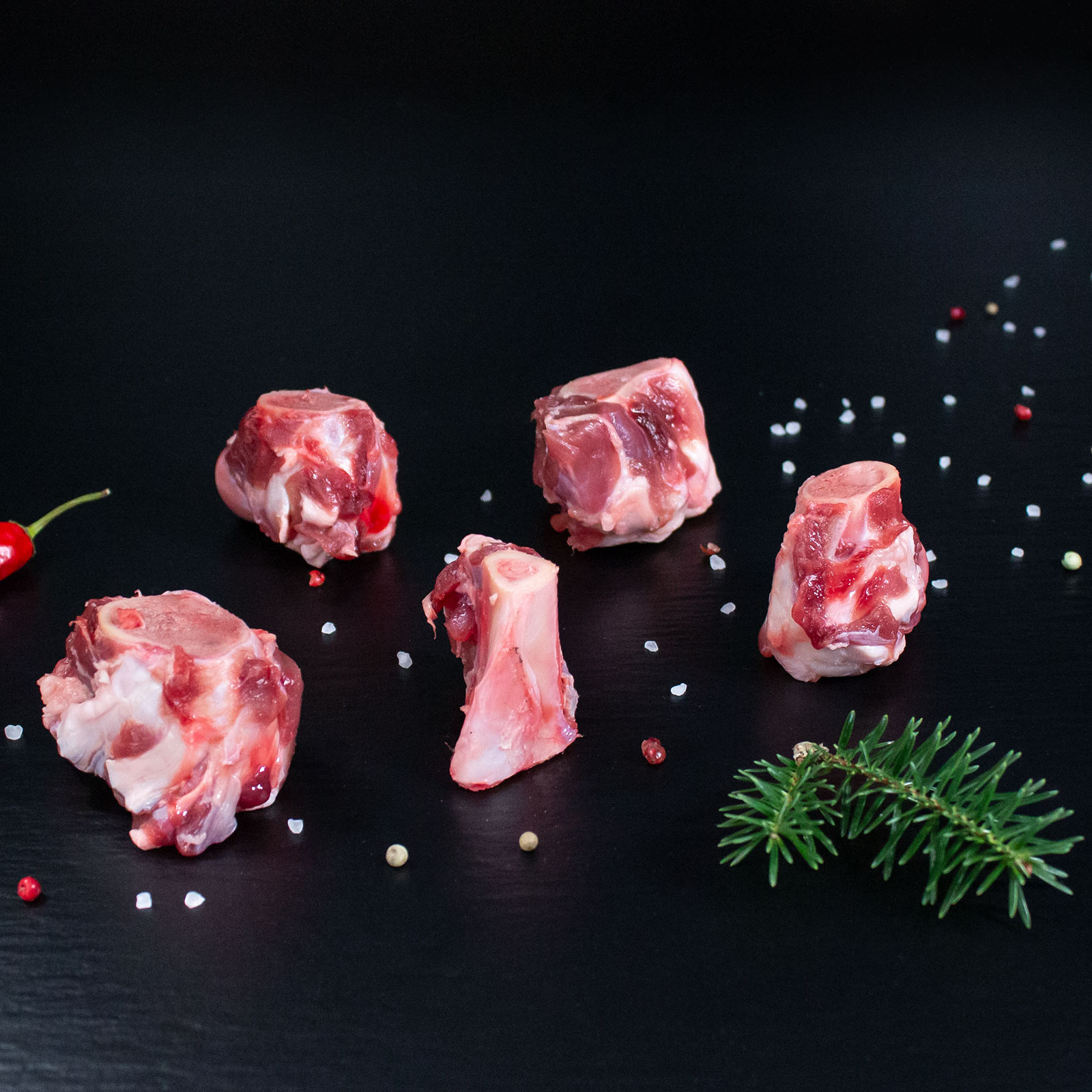 Rohe Wildschweinknochen für den Wildfond mit Pfeffer, Salz und Chili auf dunklem Untergrund