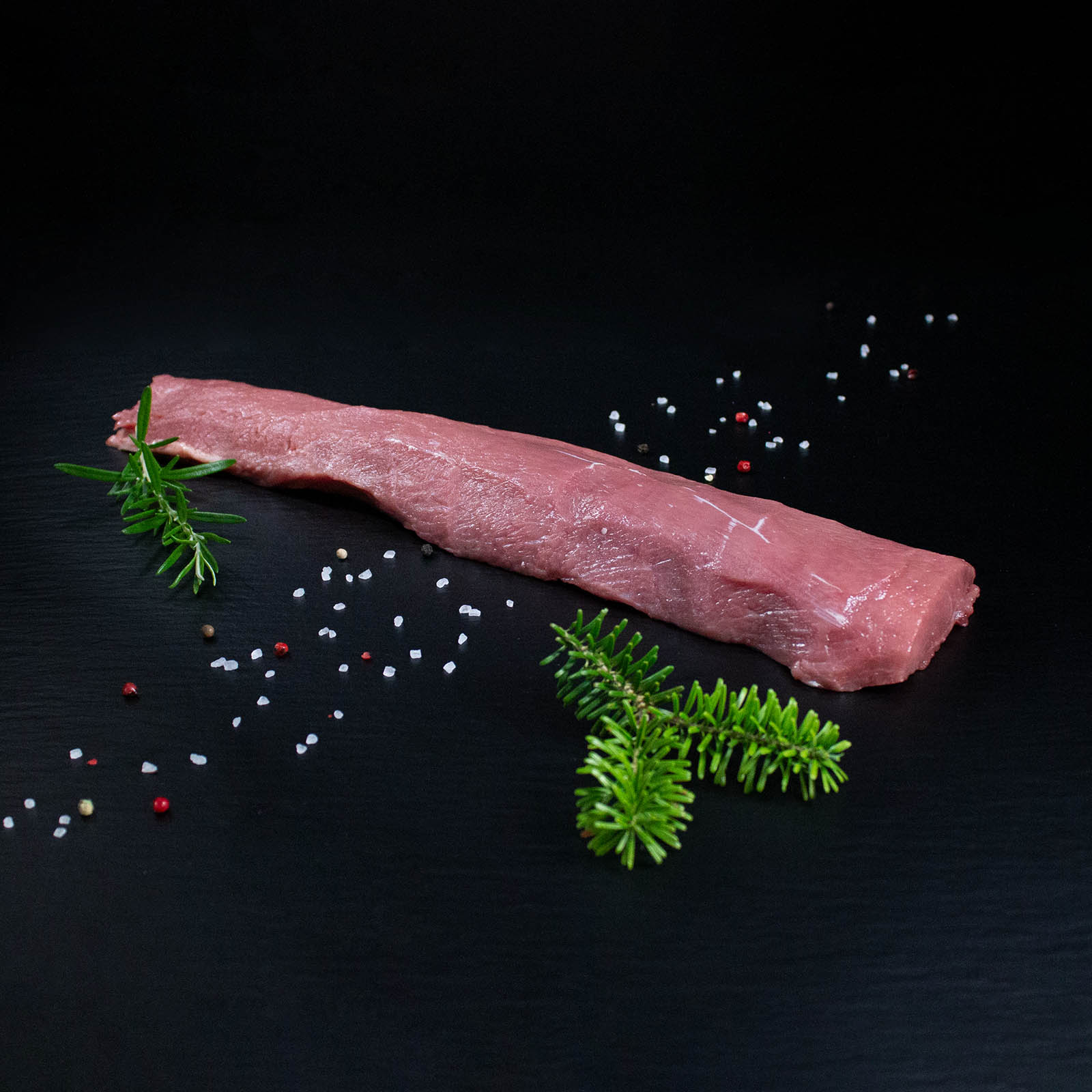 Roher parierter Wildschweinrücken ohne Knochen mit Pfeffer, Salz und Chili auf dunklem Untergrund