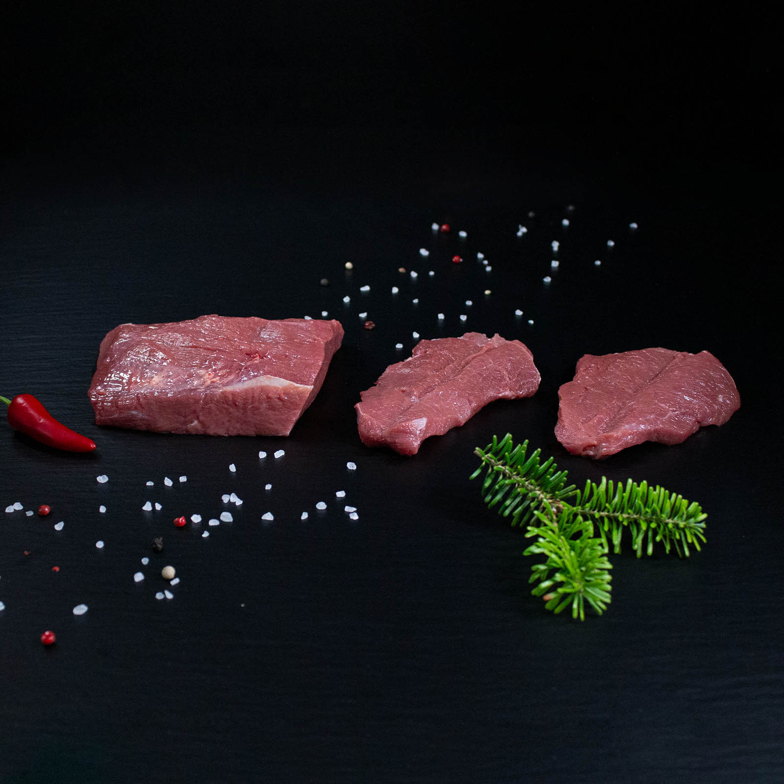 Rohe Wildschweinschnitzel mit Kräutern und Gewürzen auf dunklem Untergrund