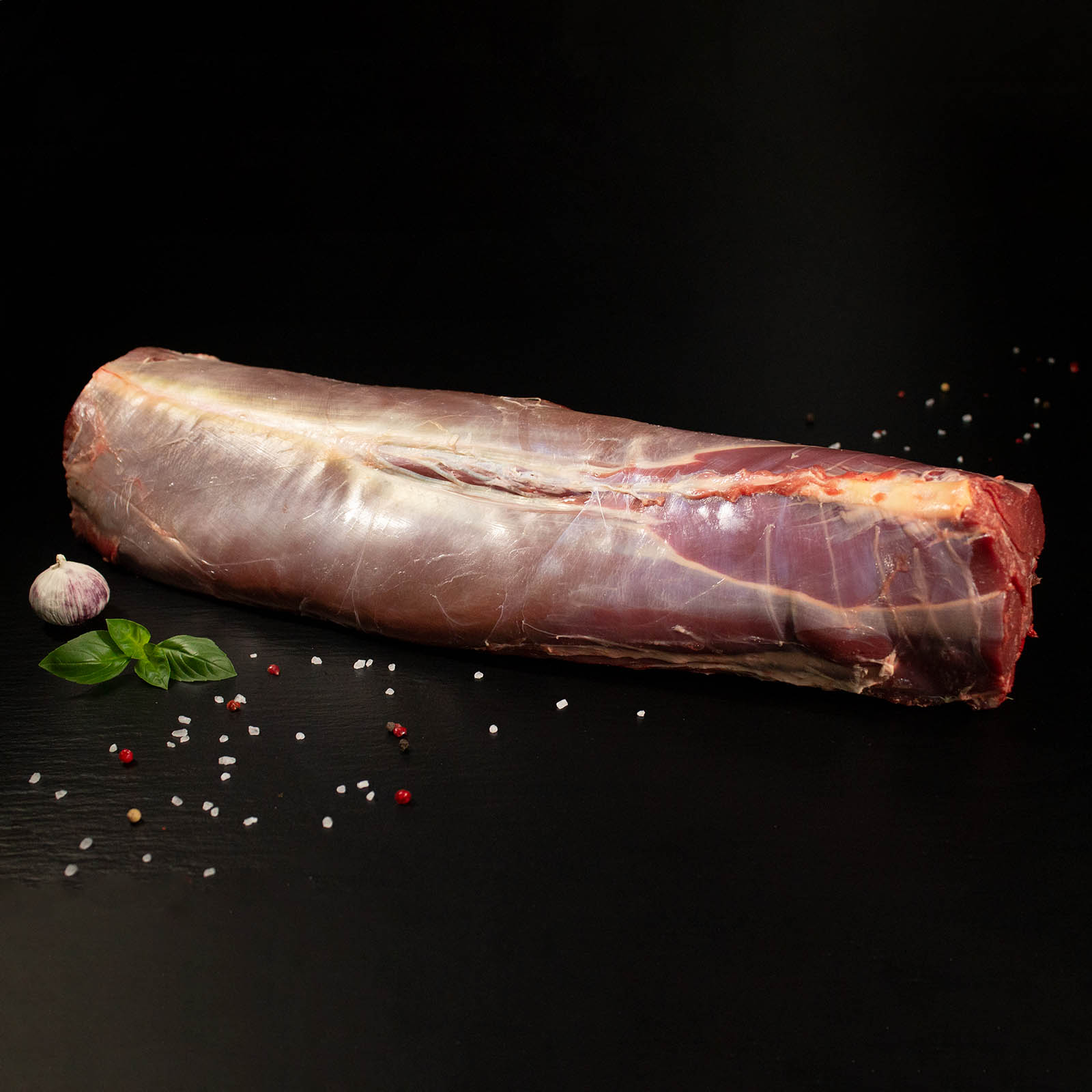 Roher Rehrücken mit Knochen, Pfeffer, Salz und Chili auf dunklem Untergrund