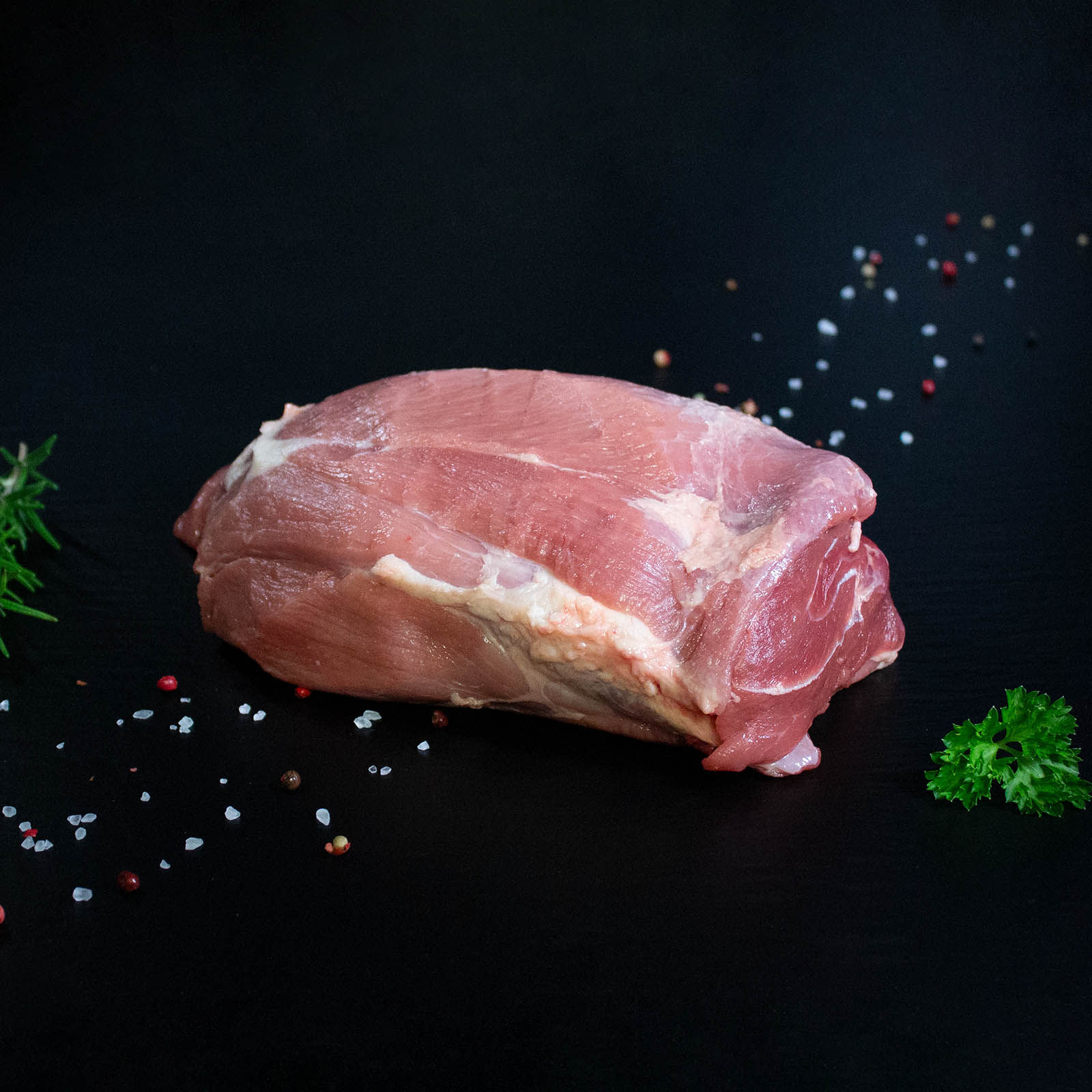Roher Wildschweinbraten aus der Keule mit Kräutern und Gewürzen auf dunklem Untergrund
