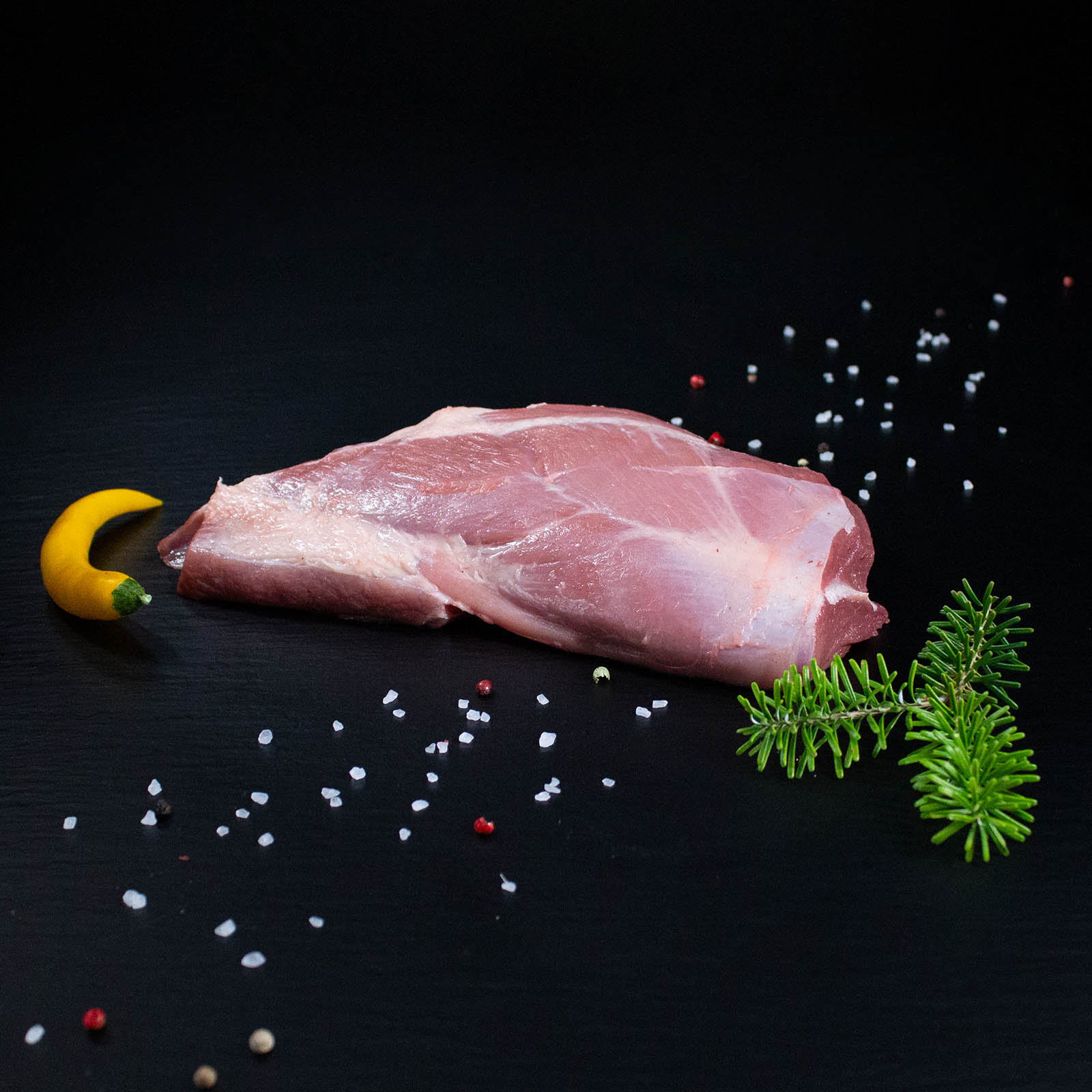 Roher Wildschweinbraten aus der Schulter mit Kräutern und Gewürzen auf dunklem Untergrund