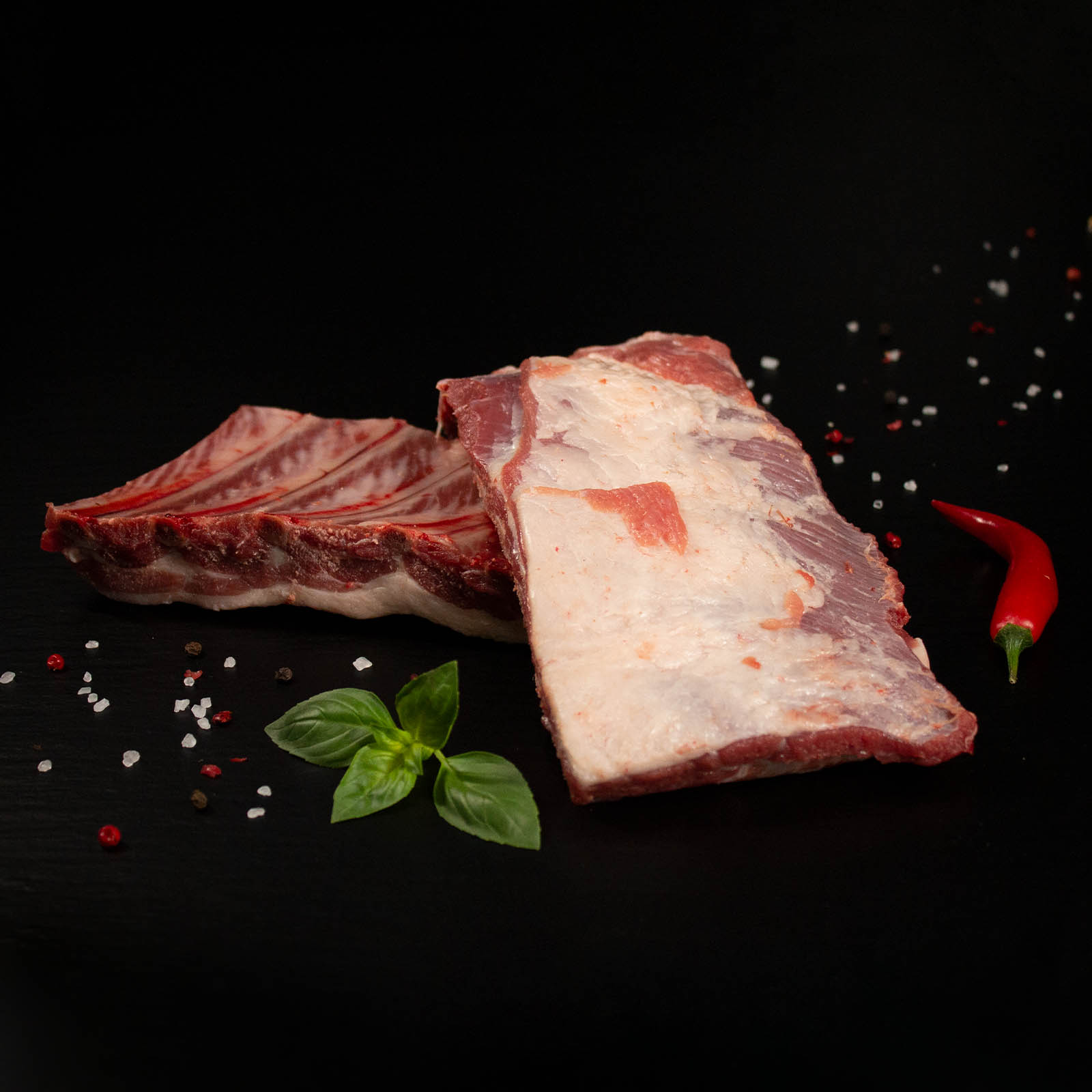 Rohe Grillrippchen vom Wildschwein mit Kräutern und Gewürzen auf dunklem Untergrund