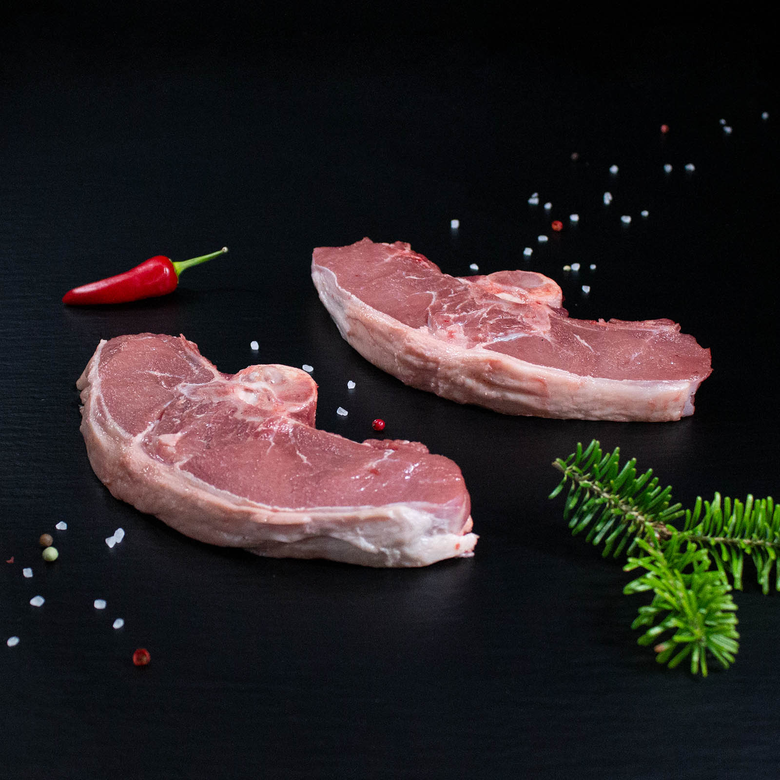 Rohes Wildschweinkotelett mit Kräutern und Gewürzen auf dunklem Untergrund