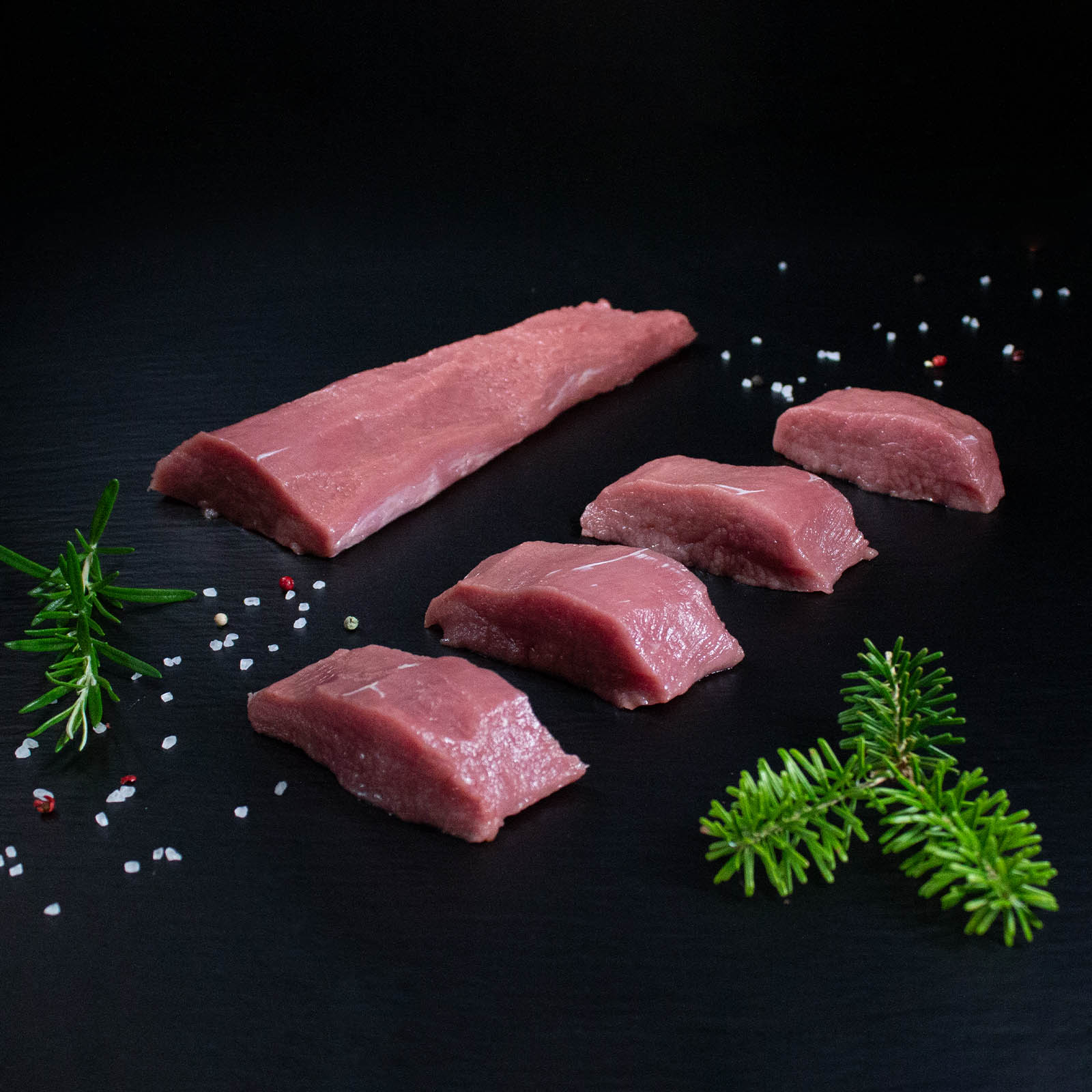 Rohe Wildschweinmedaillons mit Kräutern und Gewürzen auf dunklem Untergrund