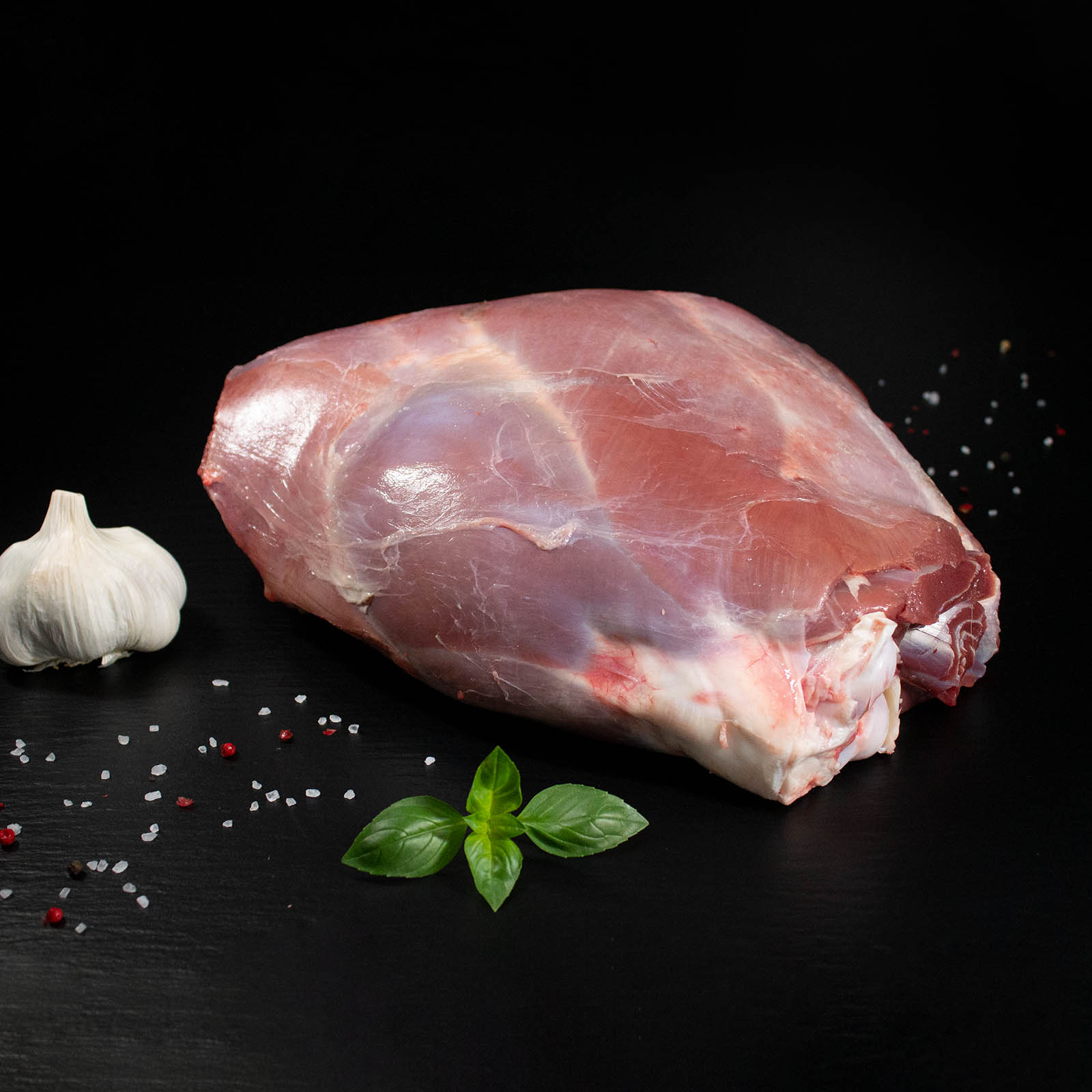 Rohe Wildschweinkeule mit Knochen, Pfeffer, Salz und Chili auf dunklem Untergrund